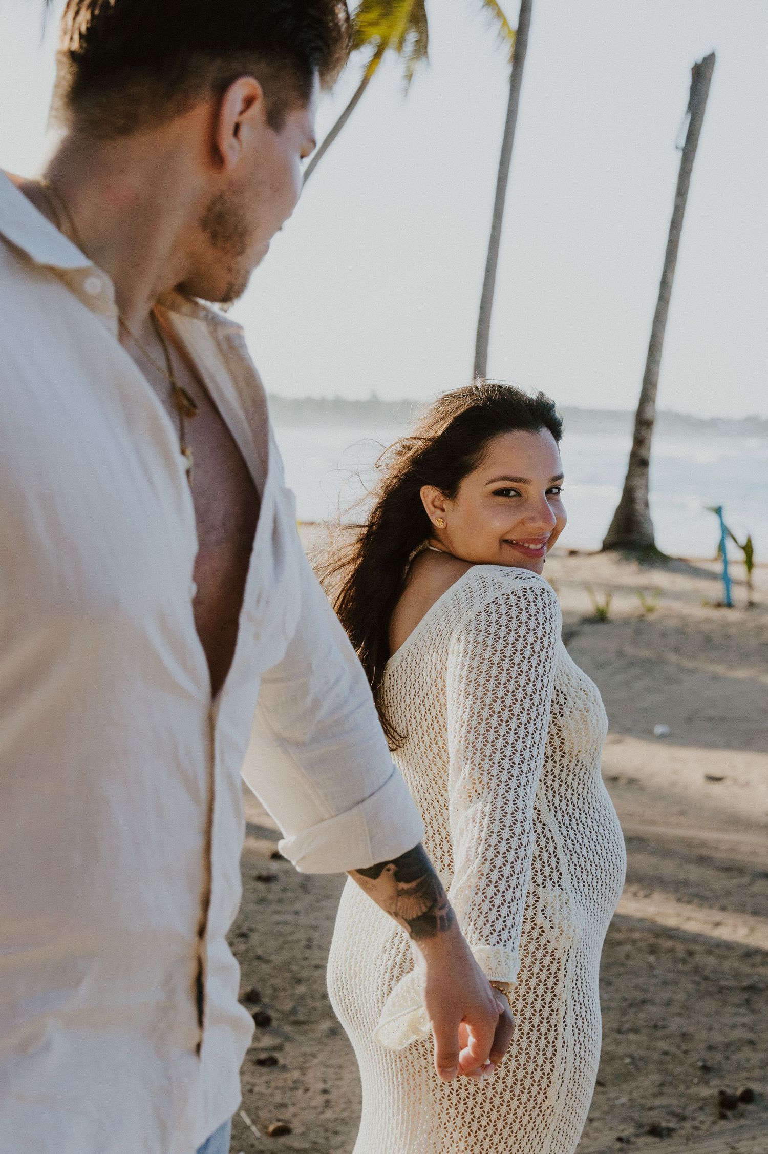 A couple sharing a romantic moment on a beach with palm trees and ocean views.