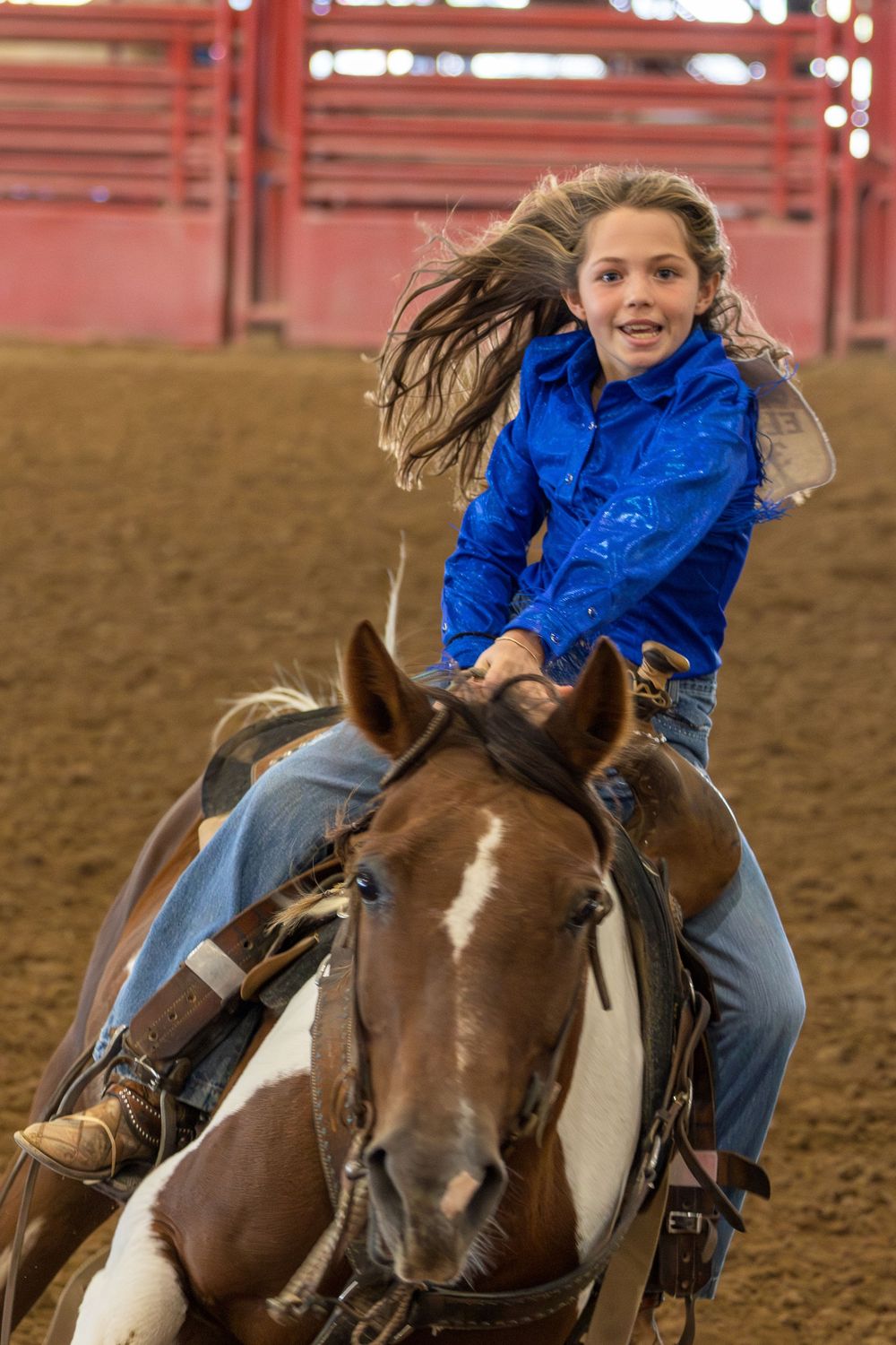 Sequence of a rider in a blue jacket performing a barrel racing run on a brown and white horse in an arena.