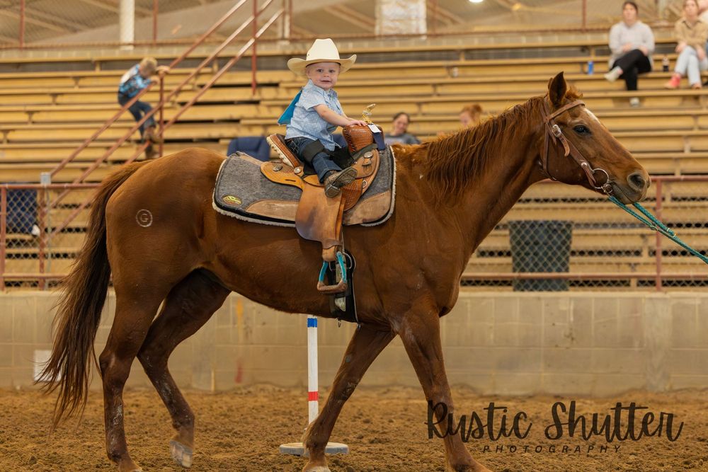 Young rider in white cowboy hat on chestnut horse at indoor Western equestrian competition.