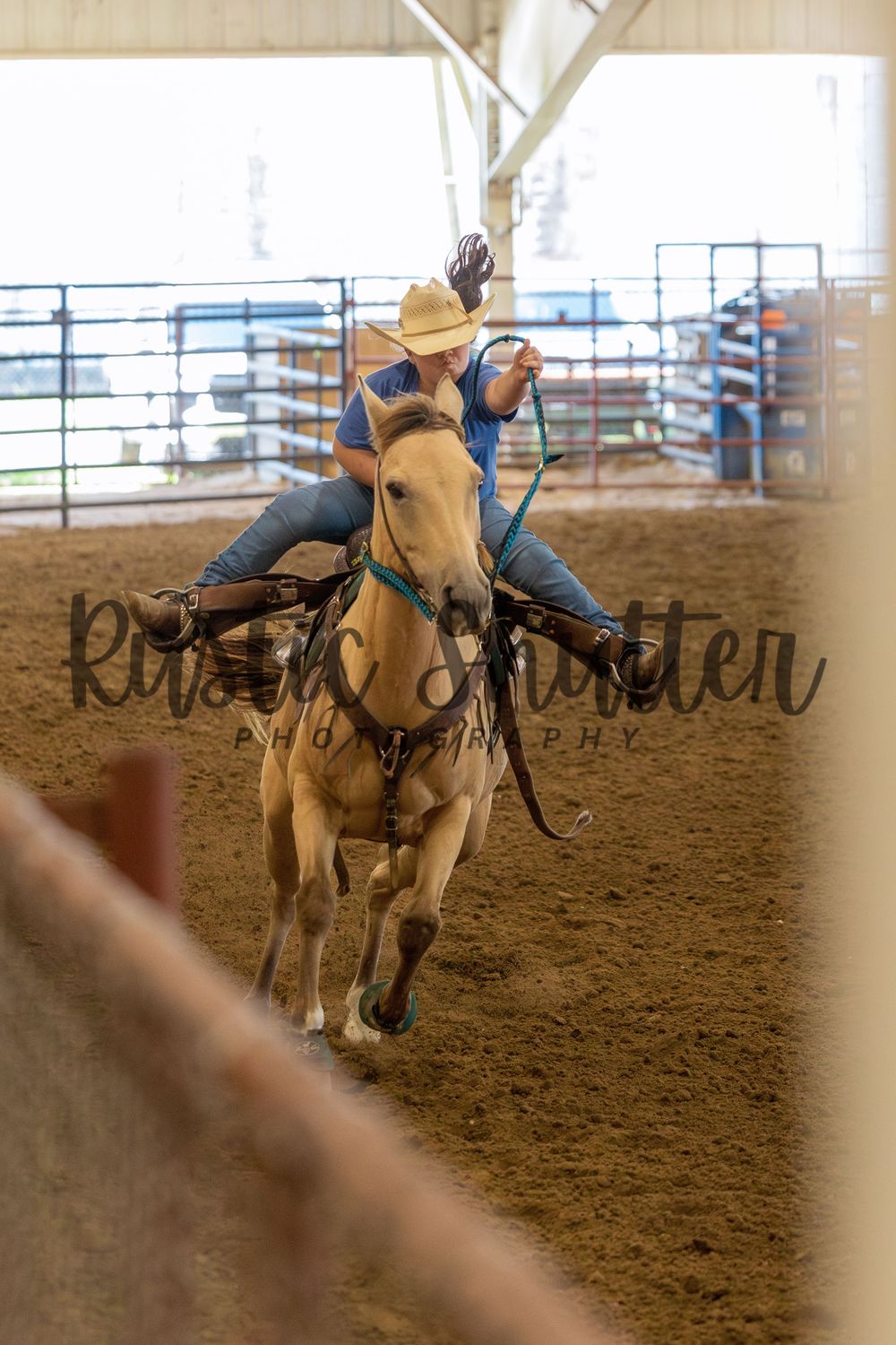 Cowboy riding a buckskin horse at full gallop inside a rodeo arena during a barrel racing event.