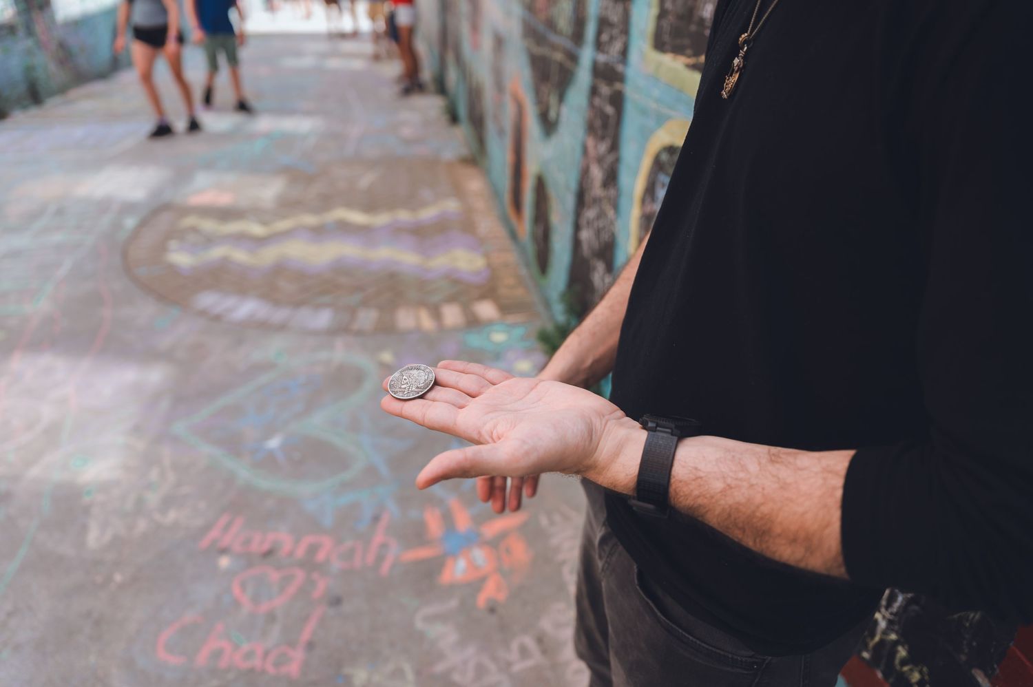 Hand wearing a black sleeve and fitness tracker extends outward against a background of colorful sidewalk chalk drawings.