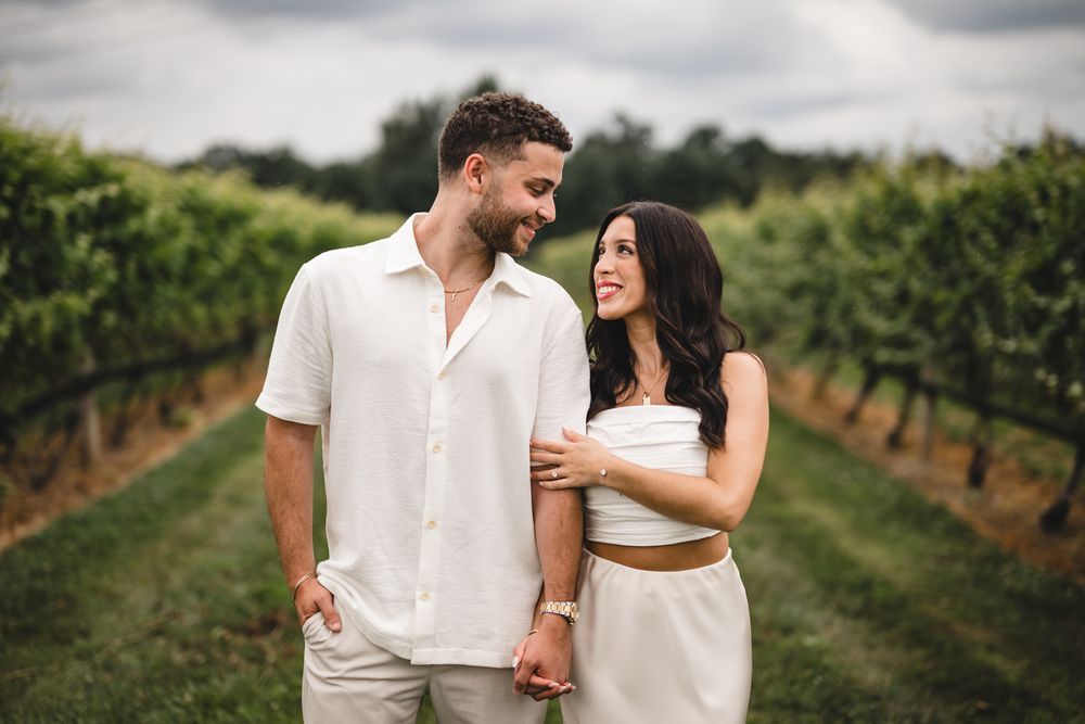 A couple in white outfits walking through scenic vineyard rows.