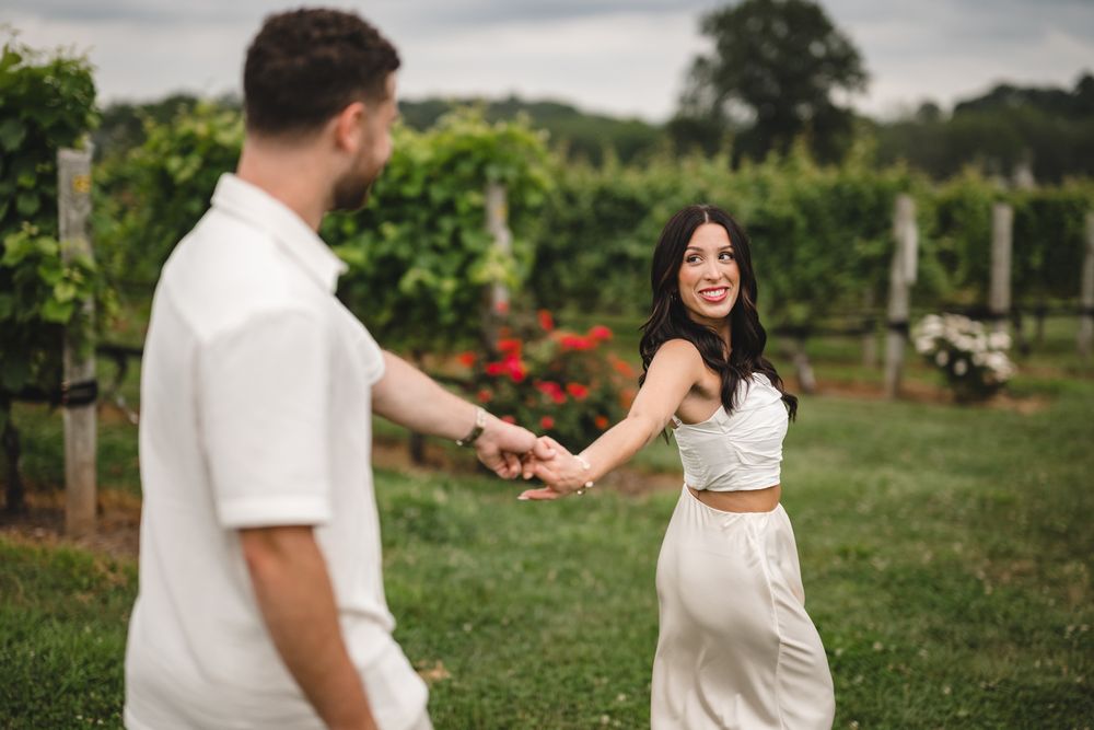 Romantic couple walking through a lush vineyard on a cloudy day.