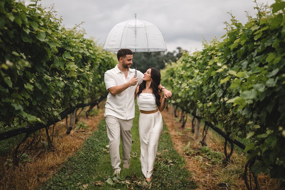 Couple strolling through vineyard rows holding a white umbrella.