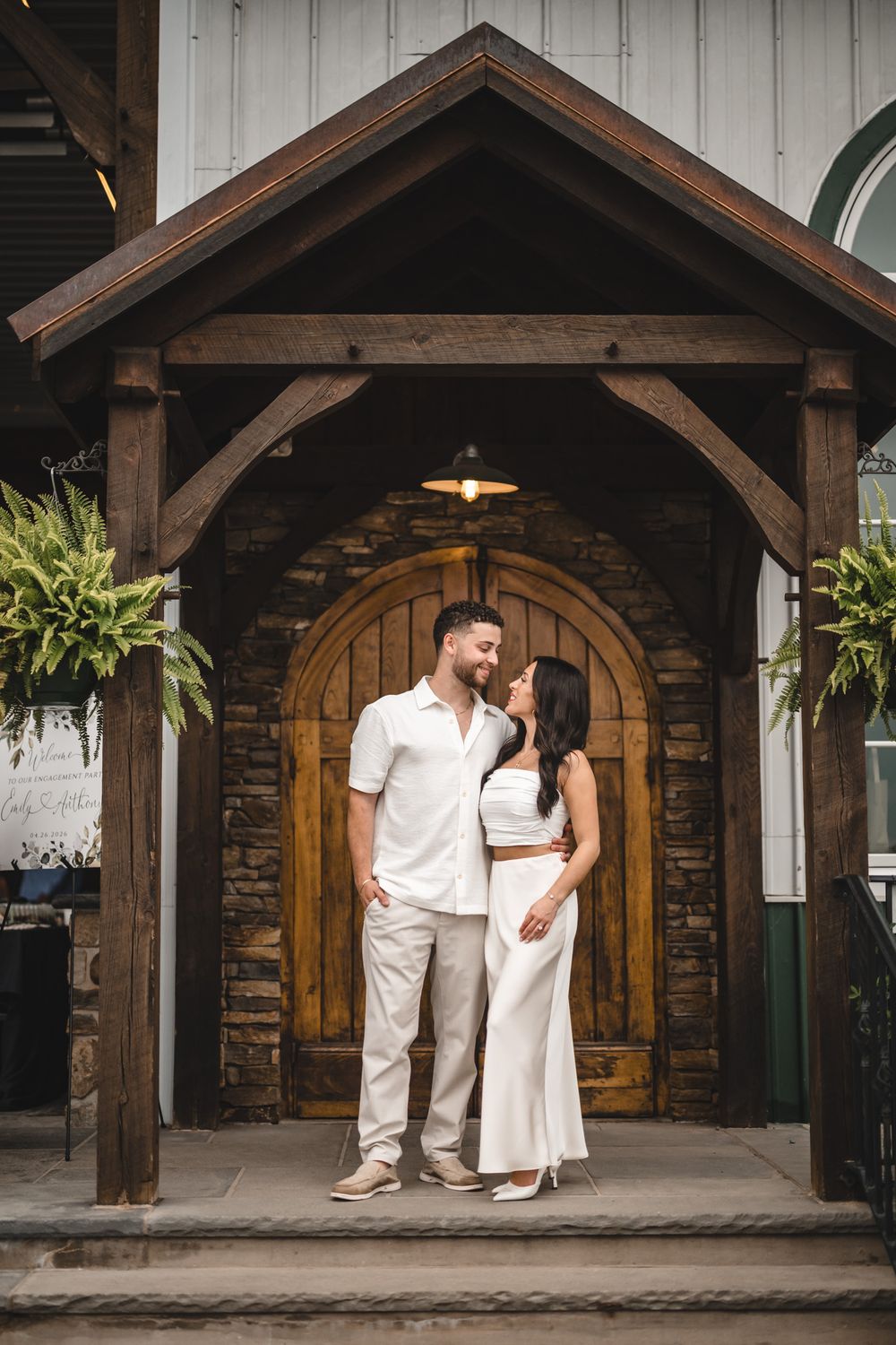 Couple in white standing under rustic wooden archway with stone accents.