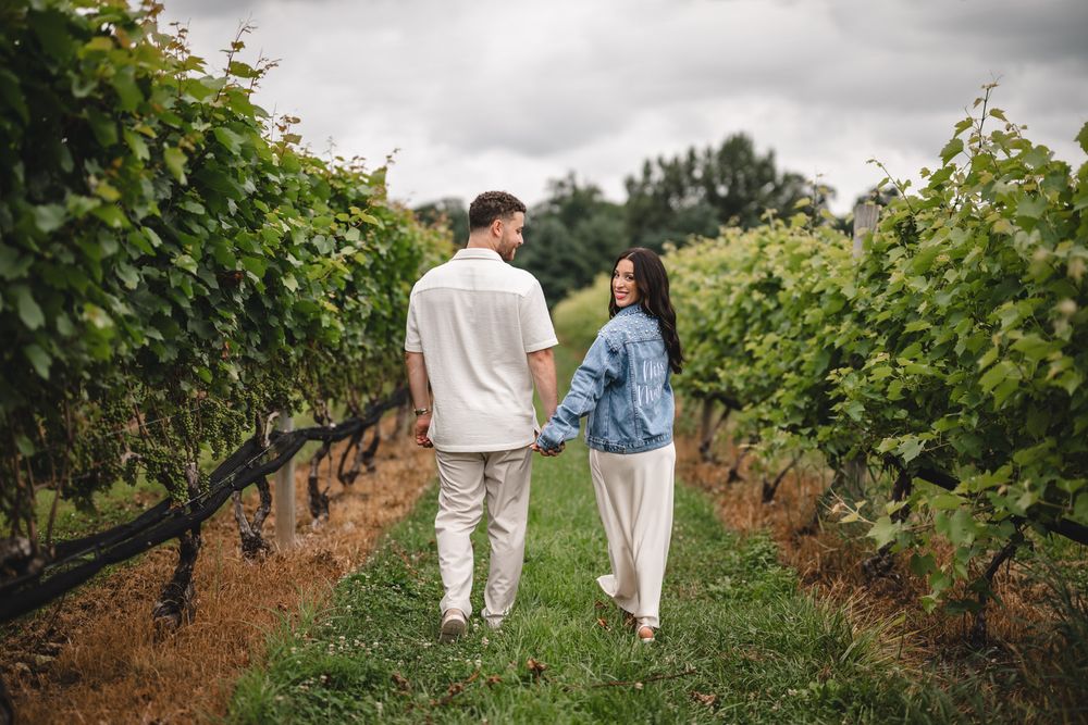 Couple walking hand in hand through rows of grapevines.
