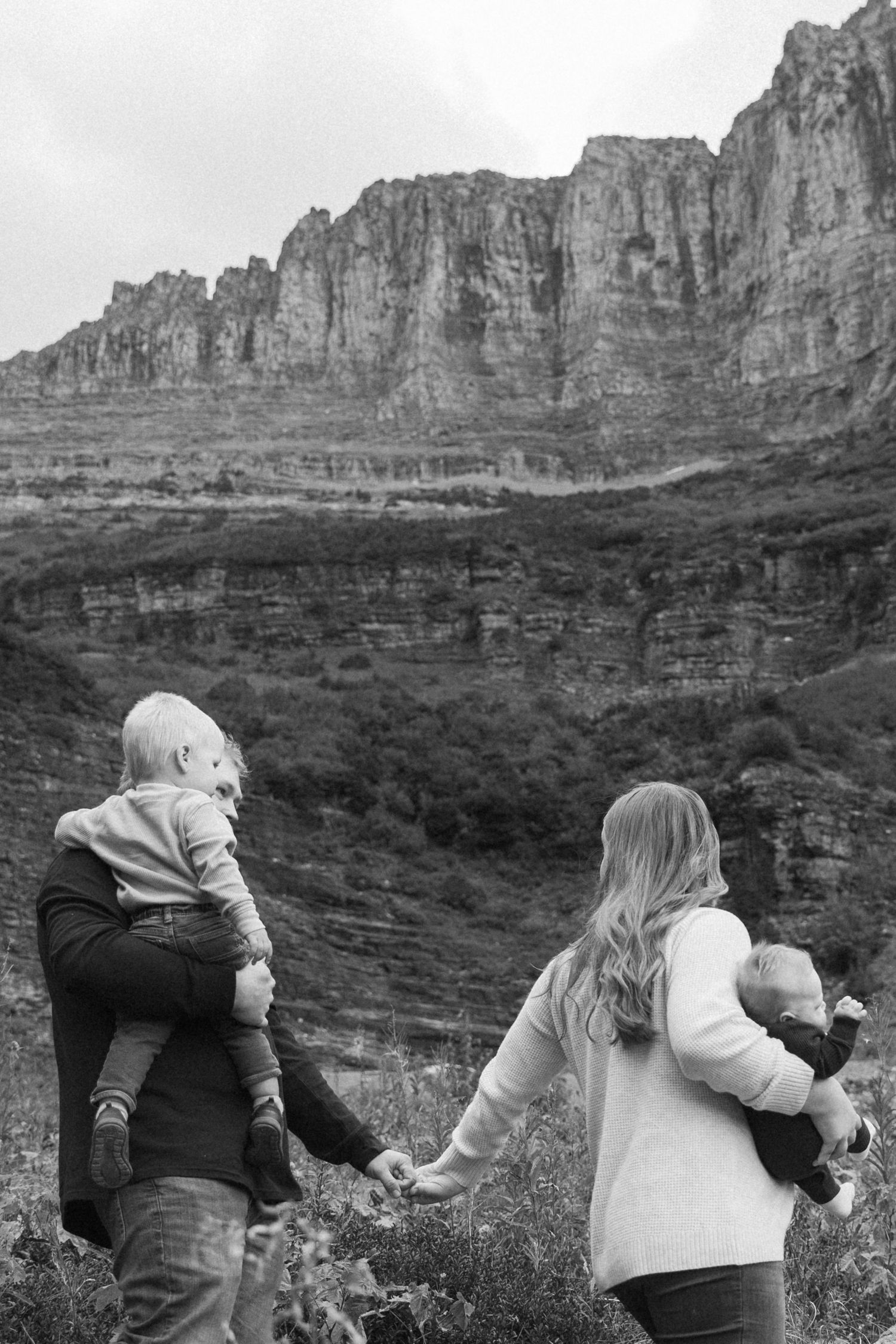 A family stands together overlooking dramatic cliffs and rock formations in a black and white landscape photograph.