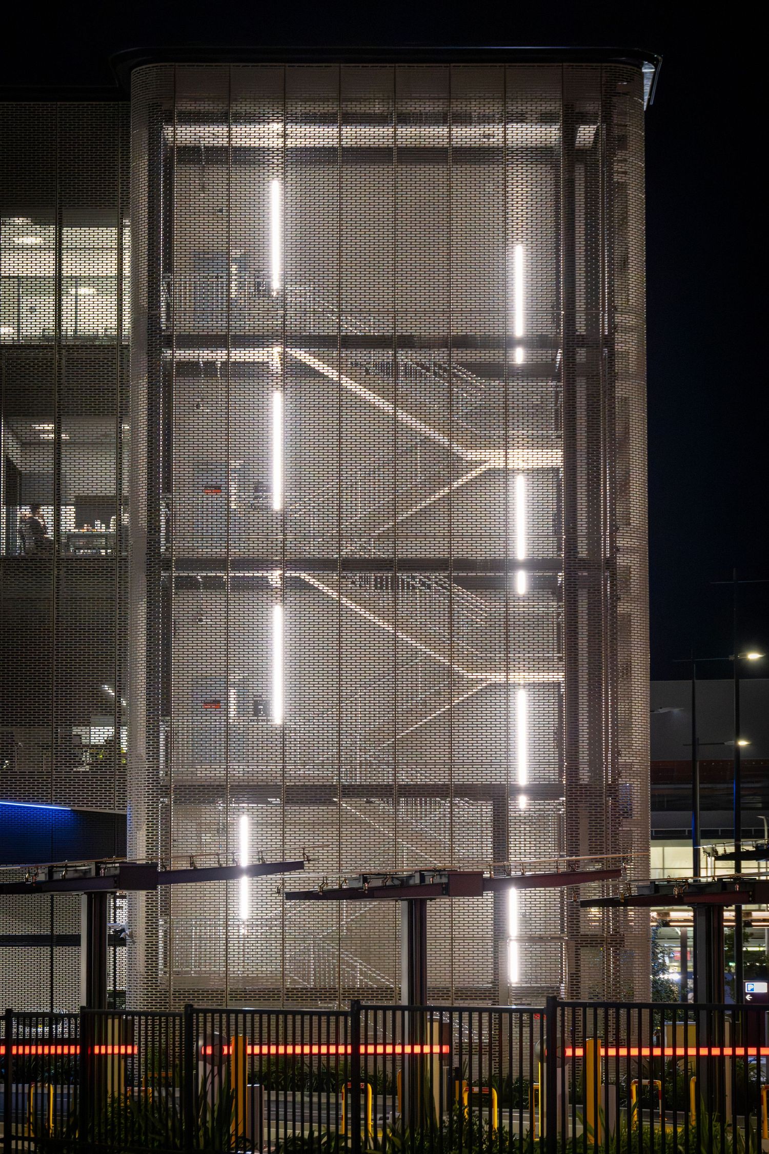 Stairwell facade at night with vertical LED strips glowing behind perforated metal mesh.