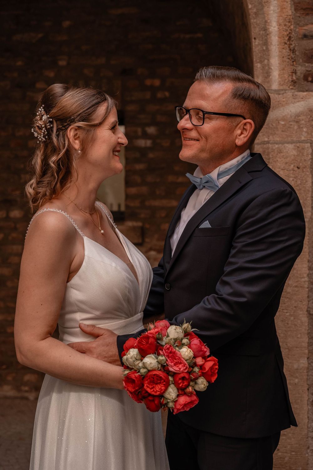 Beautiful wedding couple shares intimate moments against a brick wall backdrop with vibrant red roses.