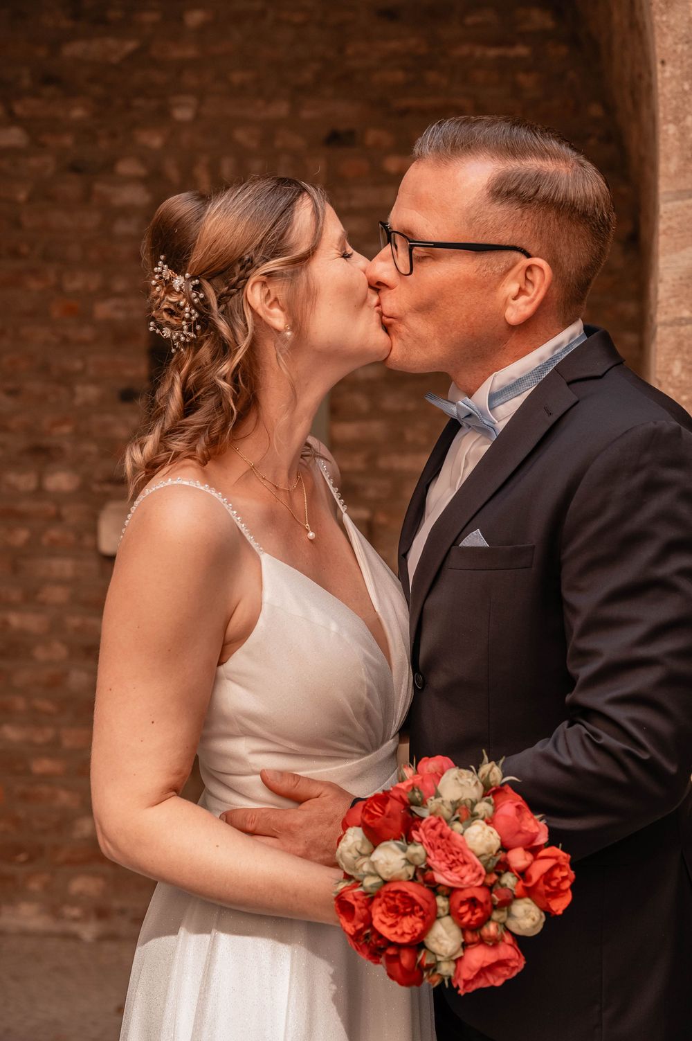A romantic wedding moment with a bridal bouquet of red roses against a brick wall backdrop.