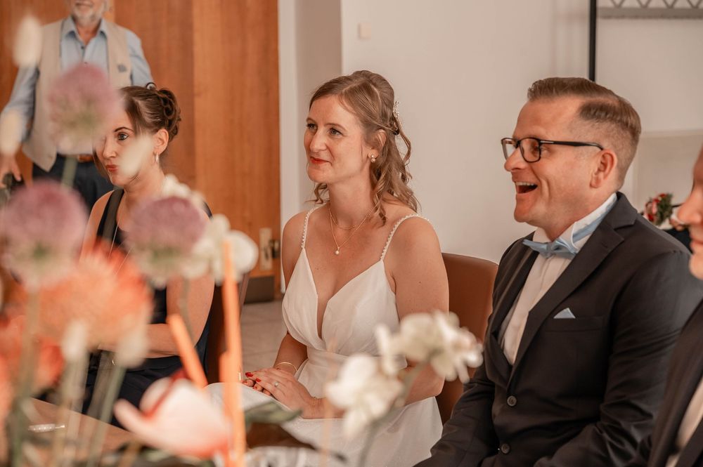 A couple shares a tender moment during their wedding reception, seated together among pink floral decorations.