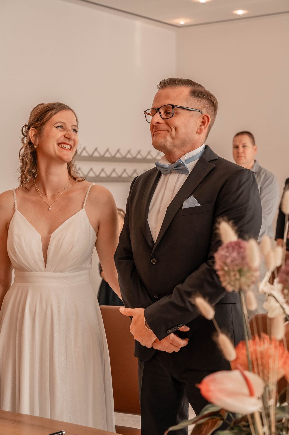 A couple shares a joyful moment during their wedding ceremony as they stand together near floral decorations.