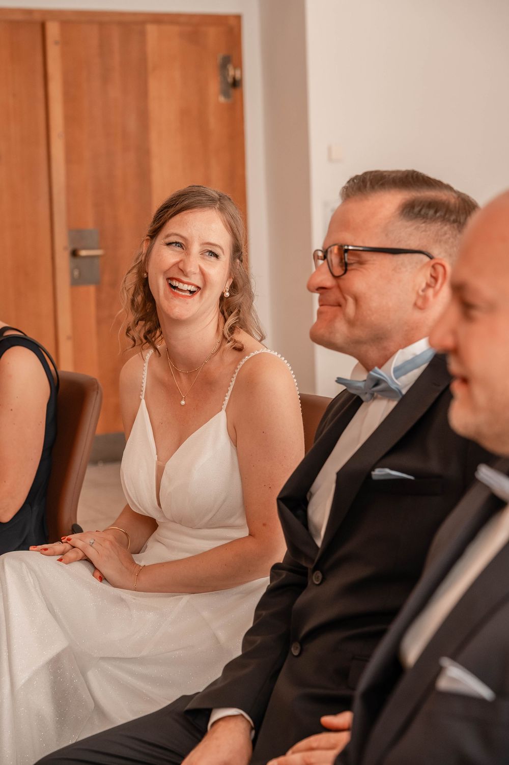 A joyful wedding scene showing a couple and guest sharing a candid moment indoors.