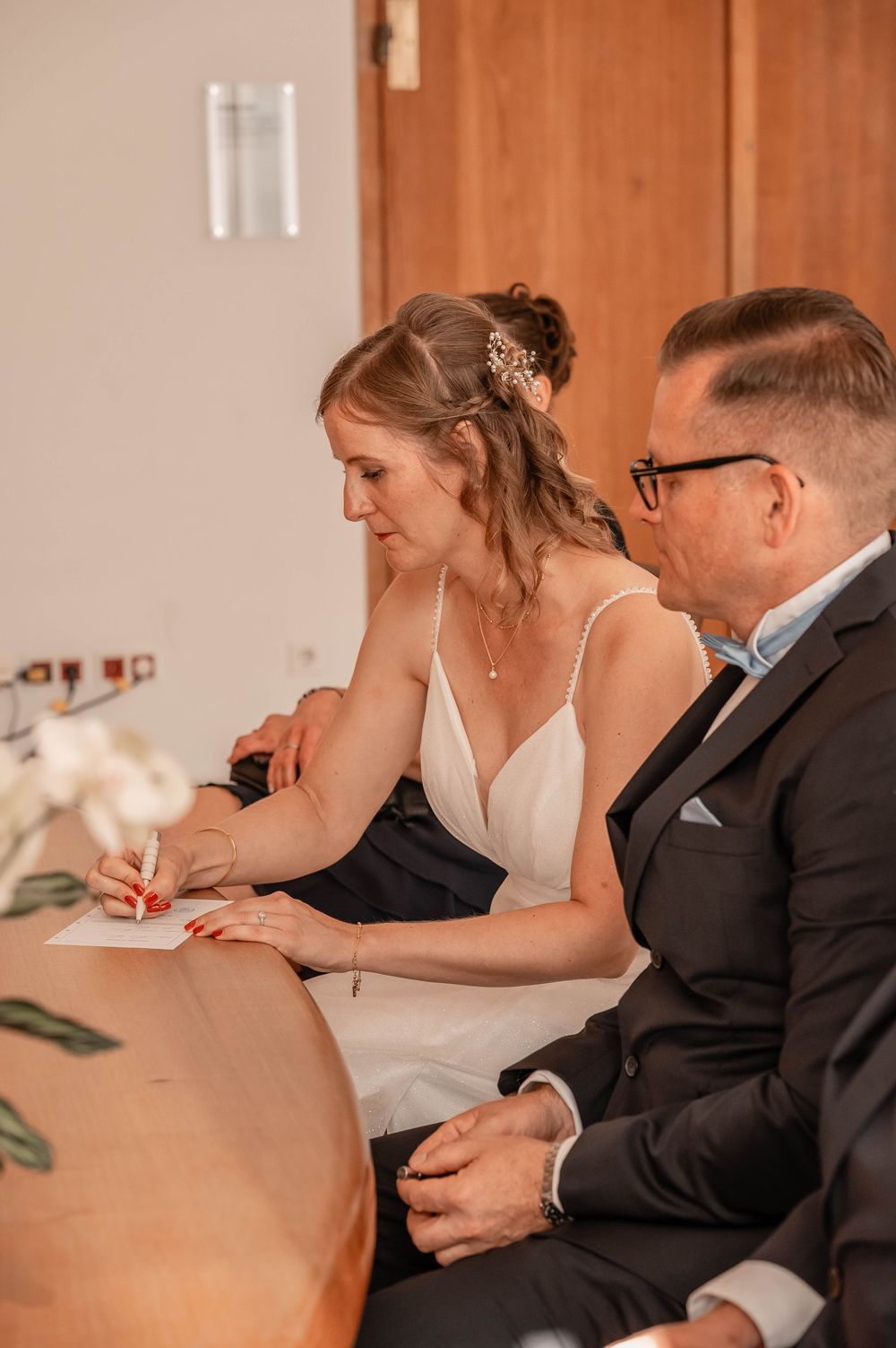 A couple sits at a table signing documents during their wedding ceremony.