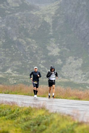 Two runners competing in a mountain trail race along a scenic mountain road.
