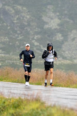 Runners making their way along a wet path through foggy mountains with grass on either side.
