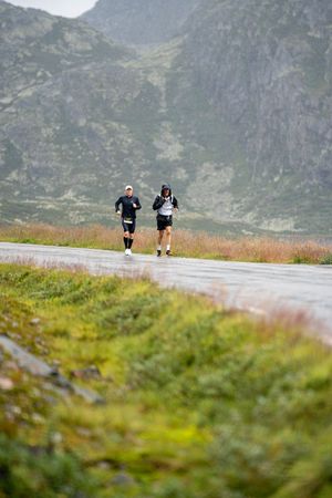 Athletes running on a wet mountain path during an endurance race in rugged terrain.