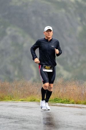 Runner wearing black athletic gear and compression socks competes on a wet mountain road during a race.