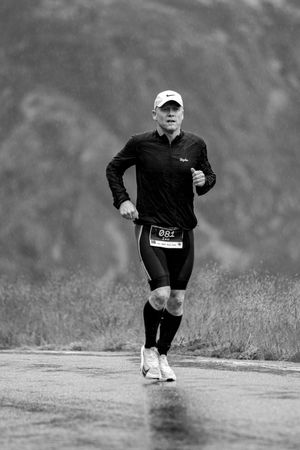 Low angle motion shot of a runner's legs splashing through puddles on a wet path during a rainy workout.