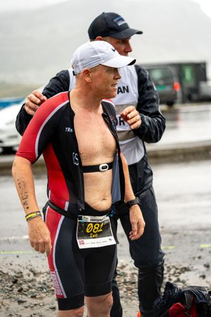Triathlete in red and black race gear getting assistance during a rainy competition.