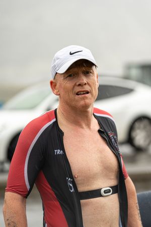 Athlete in triathlon gear with heart rate monitor and Nike cap stands after competition.