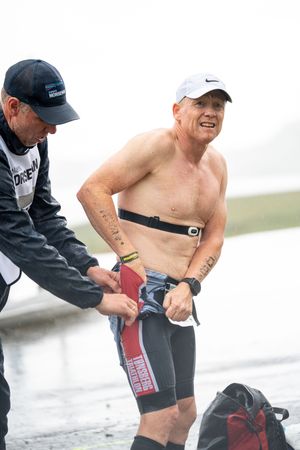 Race participant receives support from volunteer while changing gear during wet competition.