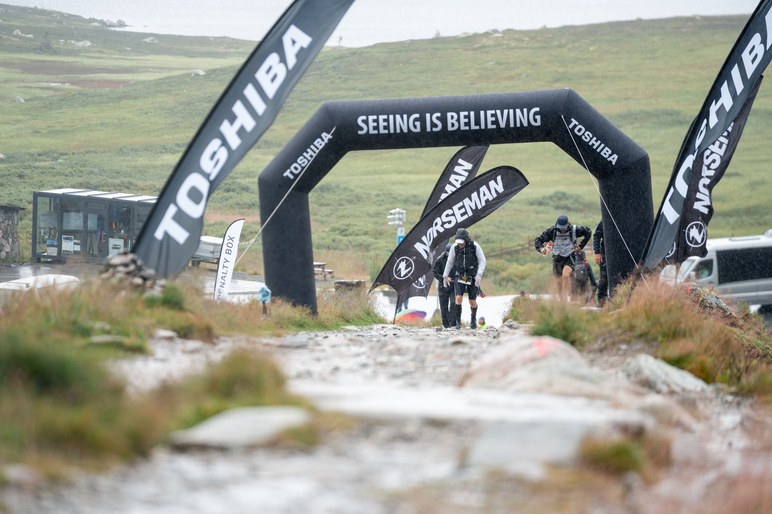 Multiple Toshiba branded arch gates set up on rocky terrain for an endurance race course.