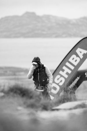 Runner stands near Toshiba banner against misty mountain backdrop during outdoor competition.