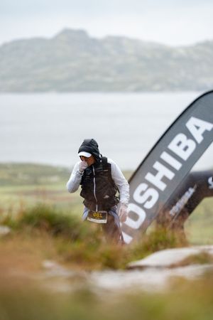 Sports photographer with camera captures event against backdrop of misty mountains and Tushiba banner.