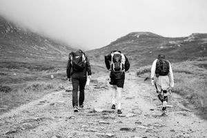 Three athletes hiking along remote mountain trail carrying backpacks in black and white photography.