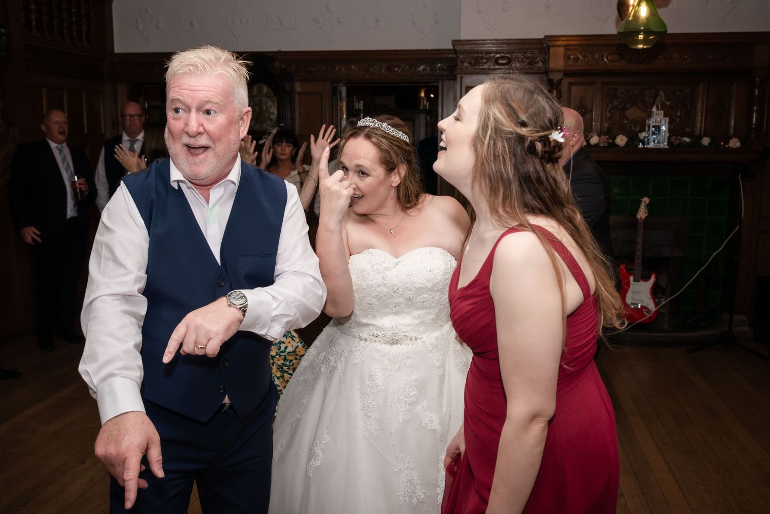 Wedding guests share a lively dance moment together at an indoor reception venue with dim lighting.