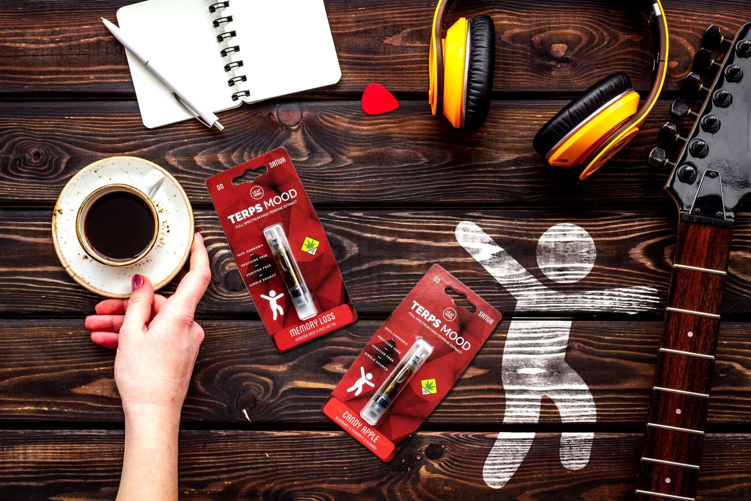 Overhead view of coffee, red Ferrari merchandise, yellow headphones and guitar on dark wooden table.