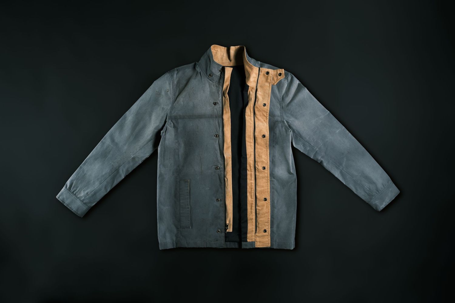 Two-tone denim jacket with contrasting tan leather panels and metal buttons displayed against dark background.