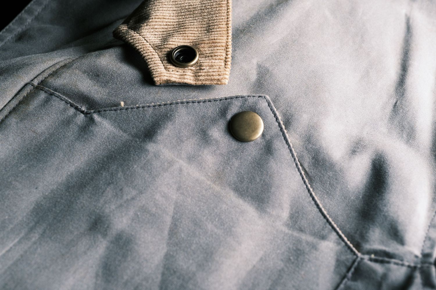 Close-up detail of gray fabric with metal snap button fastener and stitched seam.