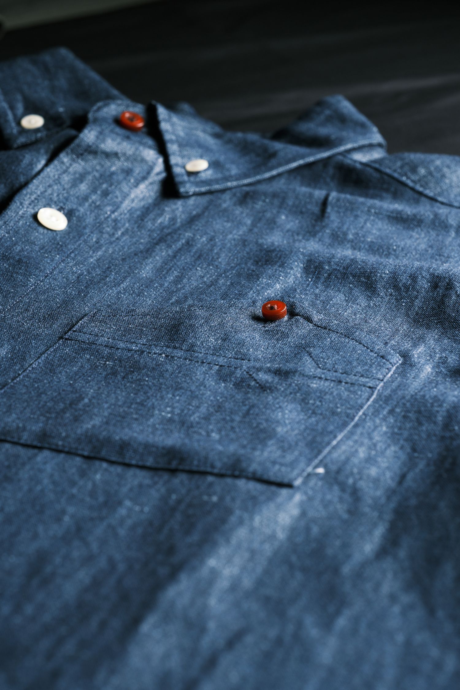 Close-up detail of a denim shirt pocket with brown wooden buttons and textured indigo fabric.
