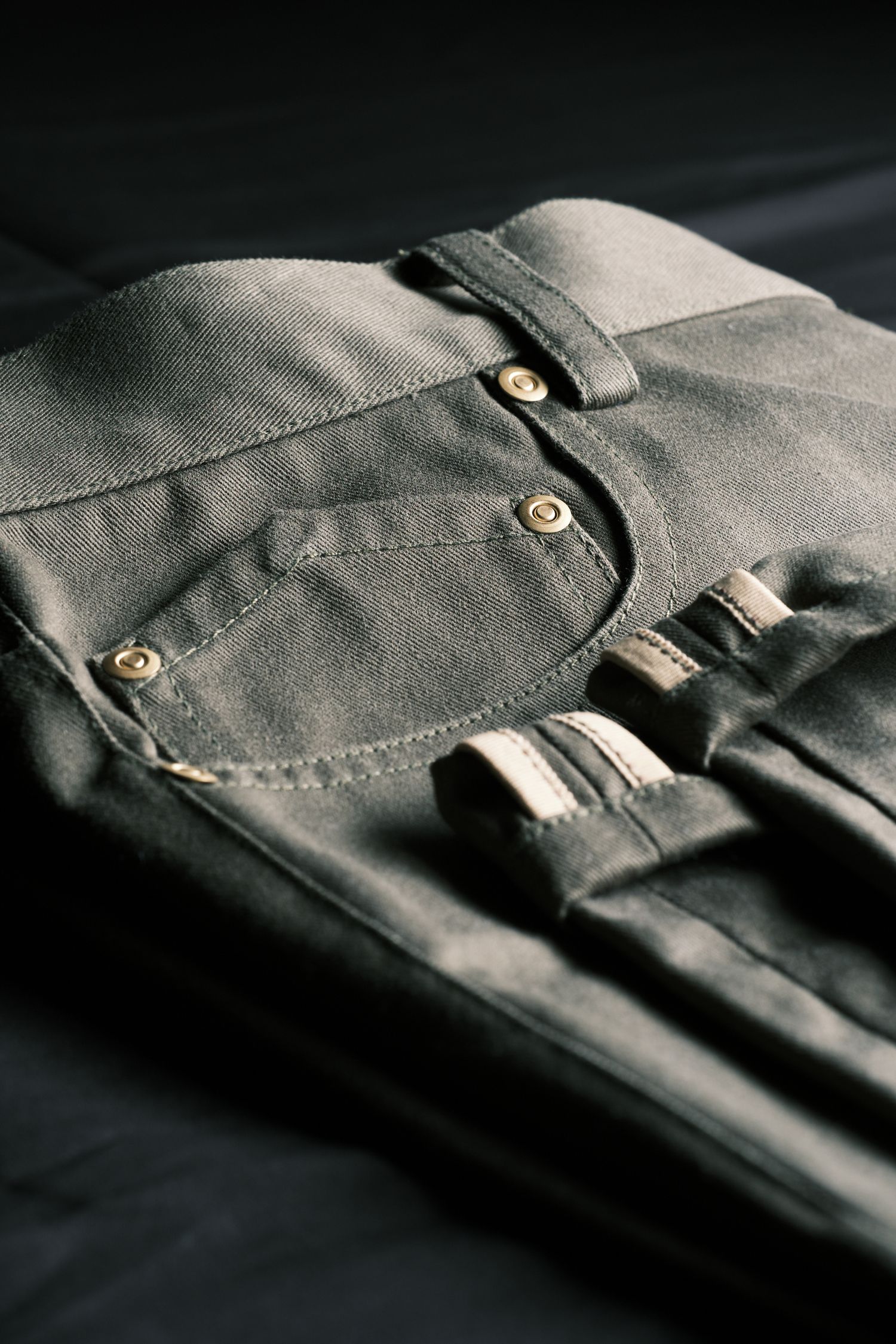 Close-up details of gray fabric garment with metal buttons and stitching showing texture and construction details.