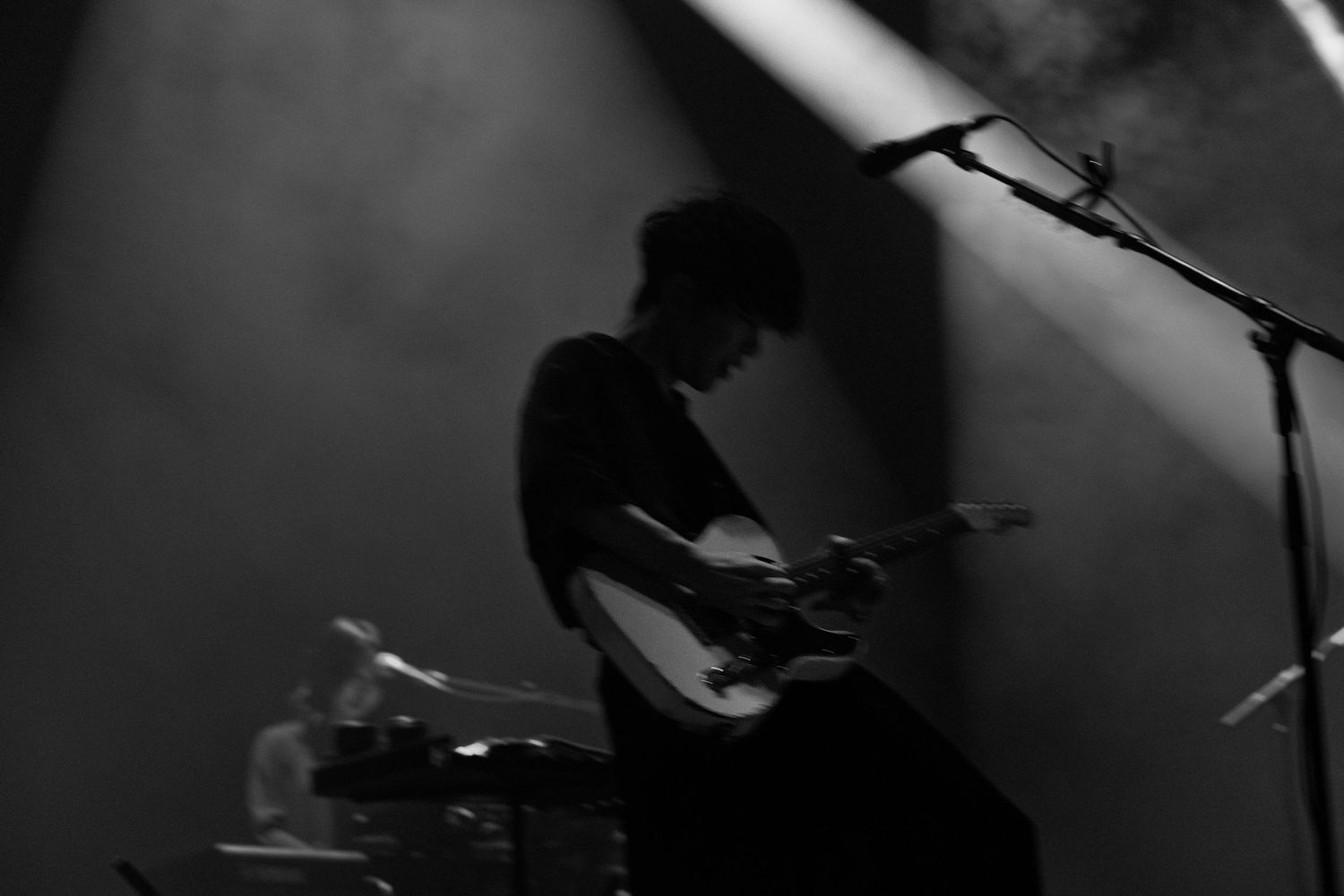 A black and white photo of TK from Ling Tosite Sigure strumming his guitar on stage at the Belasco.