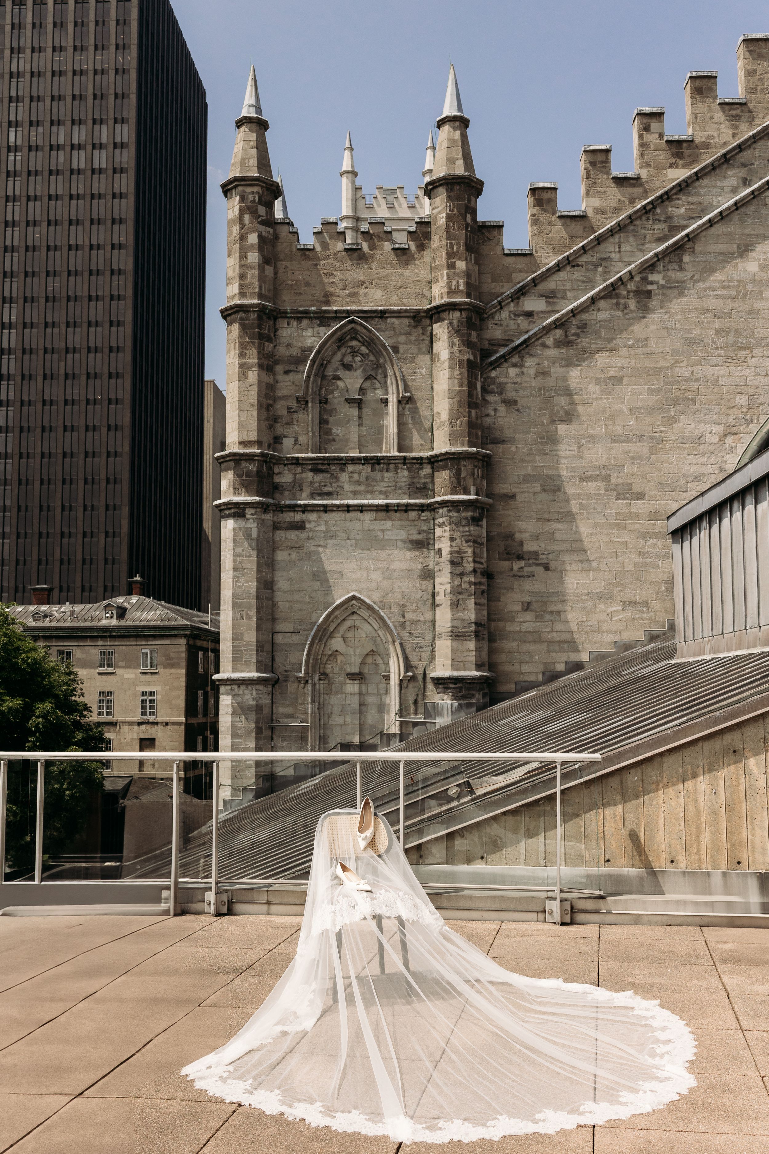 A flowing white wedding dress with long lace train photographed against a gothic cathedral facade and modern building.