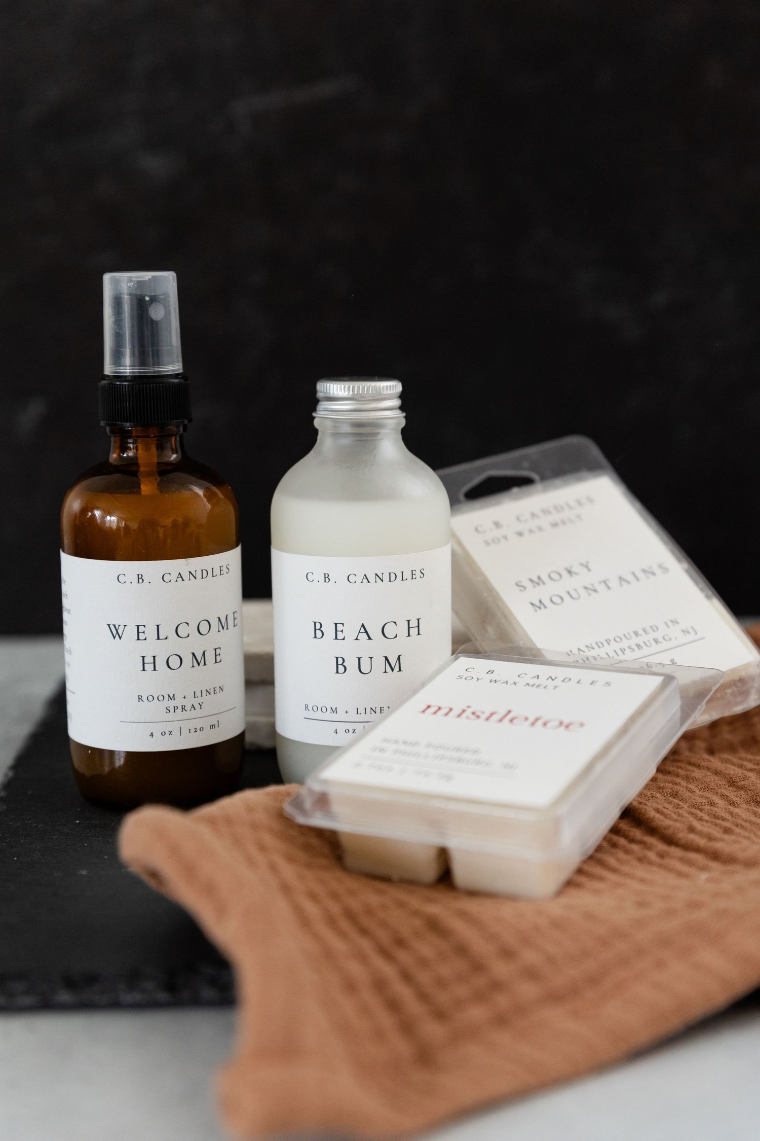 two bottles of room spray and 2 candle bars with a decorative cloth underneath
