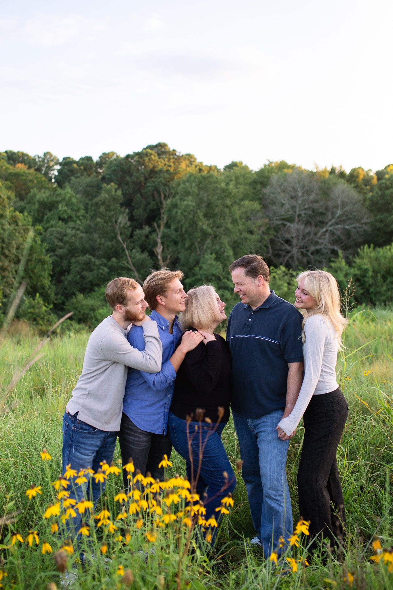 A family with adult children enjoying a candid moment together while standing in a field of yellow wildflowers at NCMA