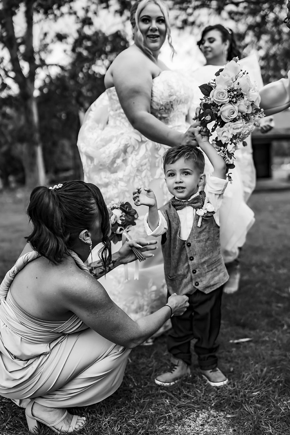 A playful sequence of a bridesmaid in a light dress bending down to interact with a young ring bearer at an outdoor wedding.