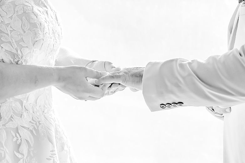 Black and white close-up of hands exchanging wedding rings during a marriage ceremony.