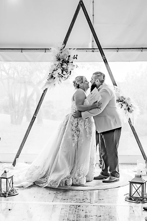 A romantic wedding couple sits together in front of a rustic A-frame backdrop with vintage lantern decorations.