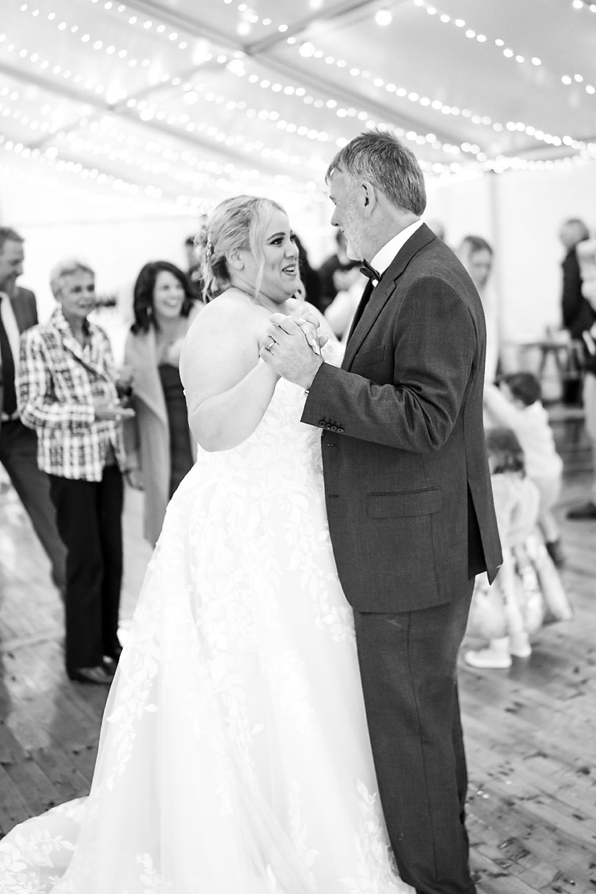 A tender black and white moment during a wedding dance in a venue decorated with string lights above.