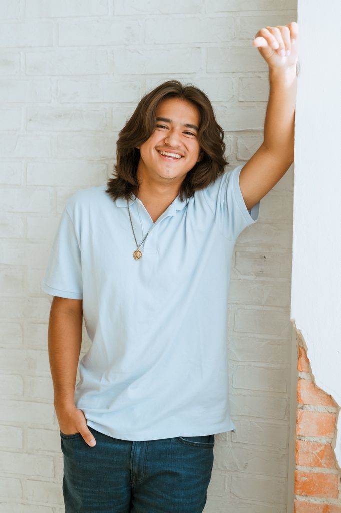 Person in light blue t-shirt and jeans poses expressively against white brick wall in three candid shots.