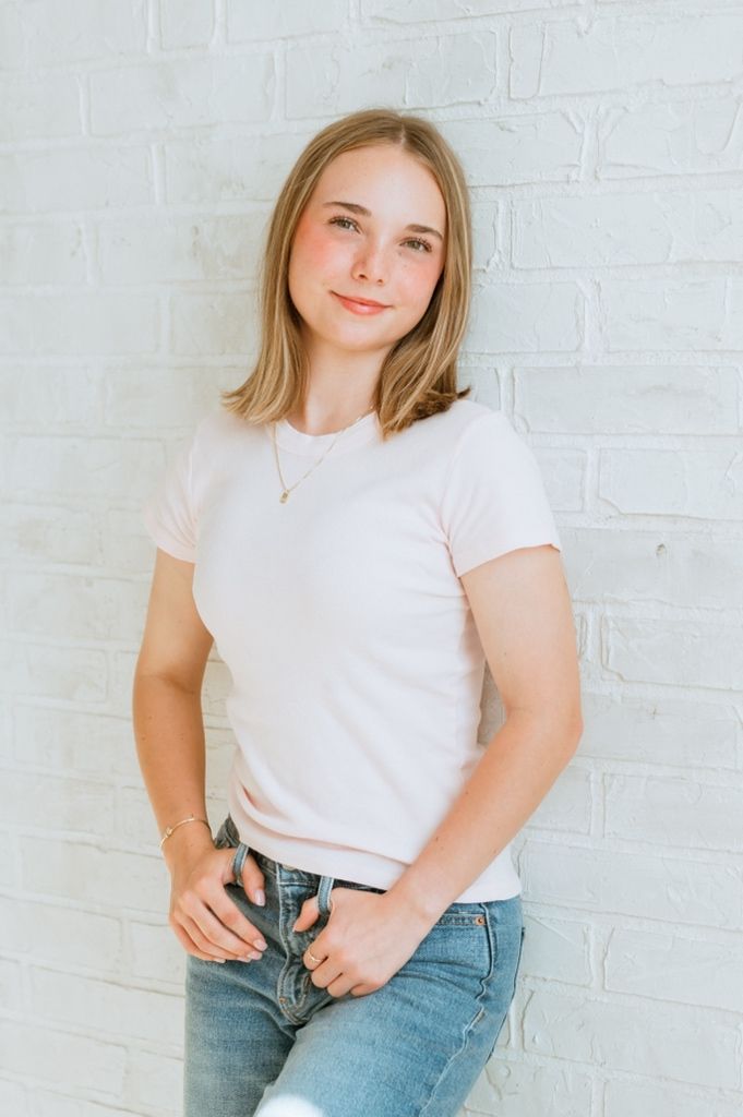 Person in white t-shirt and blue jeans poses against white brick wall in minimalist style photoshoot.