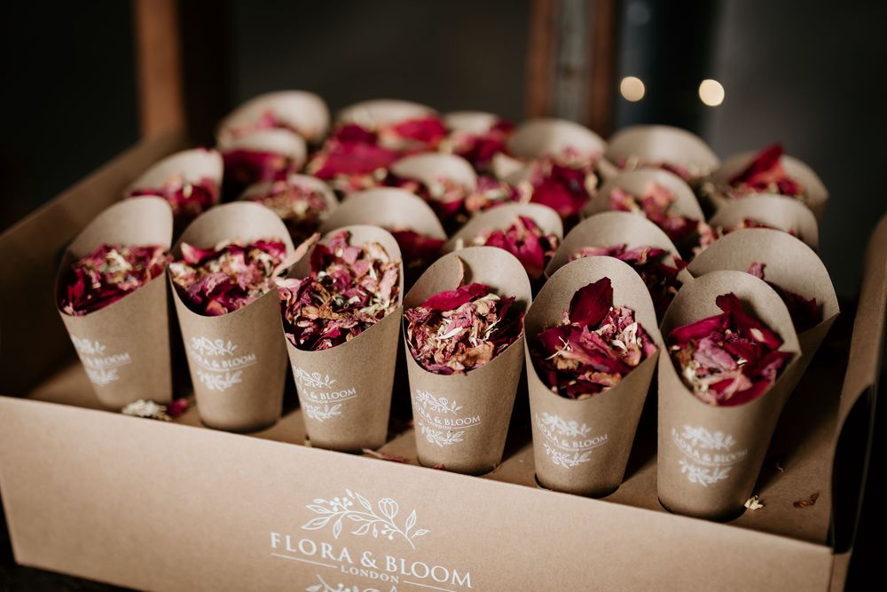 Wedding favors in wooden boxes with rose petals displayed on rustic table.