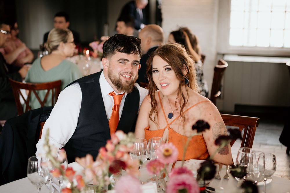 Wedding reception guests laugh and socialize at tables decorated with orange accents.
