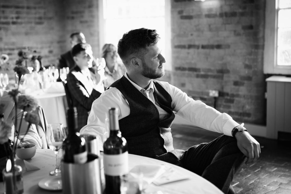 Black and white photo of wedding guests mingling at an elegant brick-walled reception venue.
