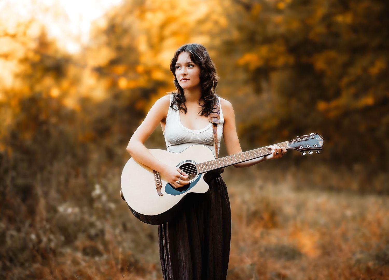 Black and white photo of a person playing an acoustic guitar in an outdoor setting with soft natural lighting.